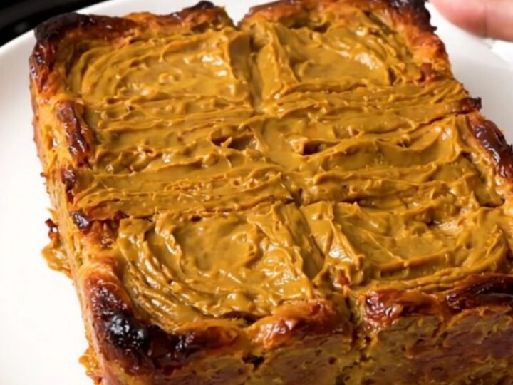 A slow cooker filled with a golden, pumpkin-spiced French toast casserole on a speckled quartz countertop.