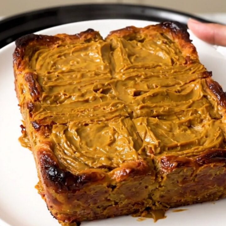 A slow cooker filled with a golden, pumpkin-spiced French toast casserole on a speckled quartz countertop.