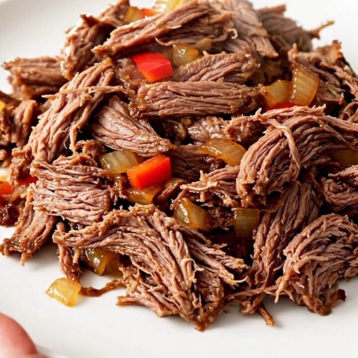 A top-down view of a black slow cooker filled with raw flank steak, sliced peppers, onions, and salsa.