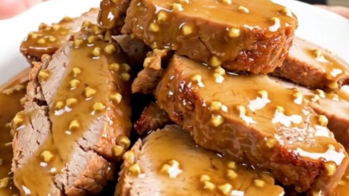 A close-up of sliced honey mustard pork tenderloin on a white plate with a glossy glaze.