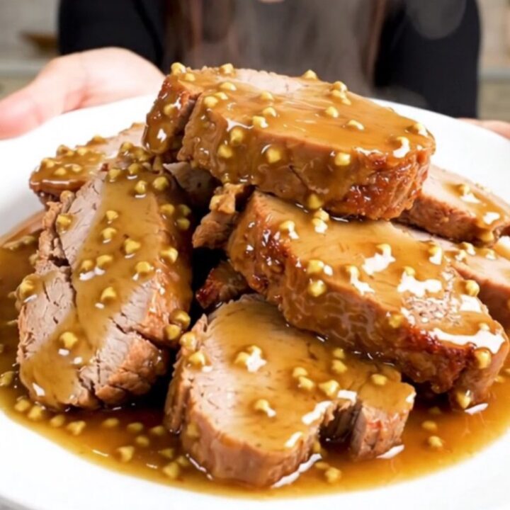 A close-up of sliced honey mustard pork tenderloin on a white plate with a glossy glaze.