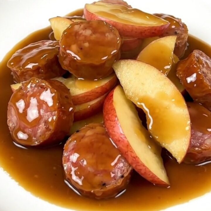 A close-up of finished maple Dijon smoked sausage and tender apple slices served on a white plate.