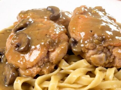 A close-up of tender chicken thighs covered in a rich, creamy mushroom gravy, served over a bed of egg noodles.