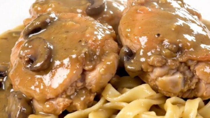 A close-up of tender chicken thighs covered in a rich, creamy mushroom gravy, served over a bed of egg noodles.