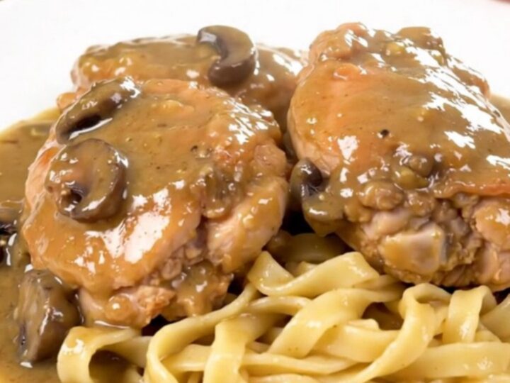 A close-up of tender chicken thighs covered in a rich, creamy mushroom gravy, served over a bed of egg noodles.