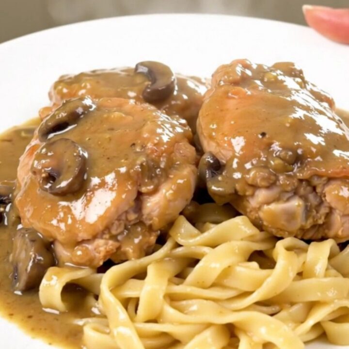 A close-up of tender chicken thighs covered in a rich, creamy mushroom gravy, served over a bed of egg noodles.