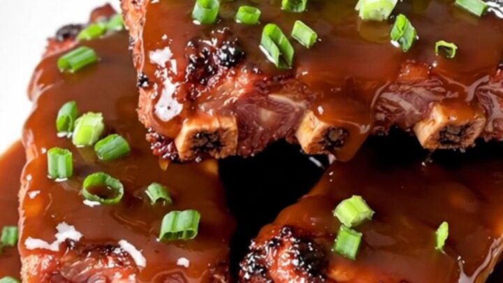 A close-up of glossy, tender baby back ribs glazed in honey barbecue sauce on a white plate.