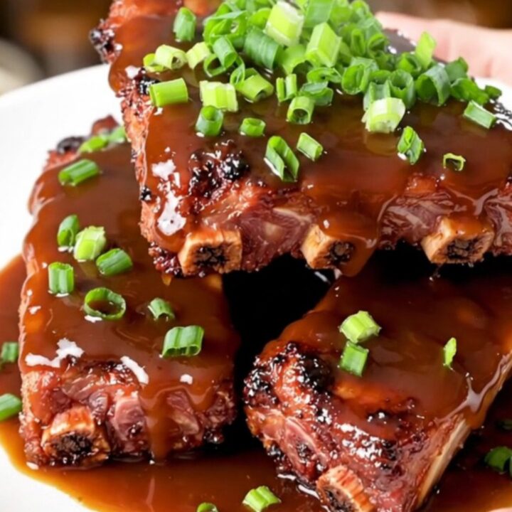 A close-up of glossy, tender baby back ribs glazed in honey barbecue sauce on a white plate.