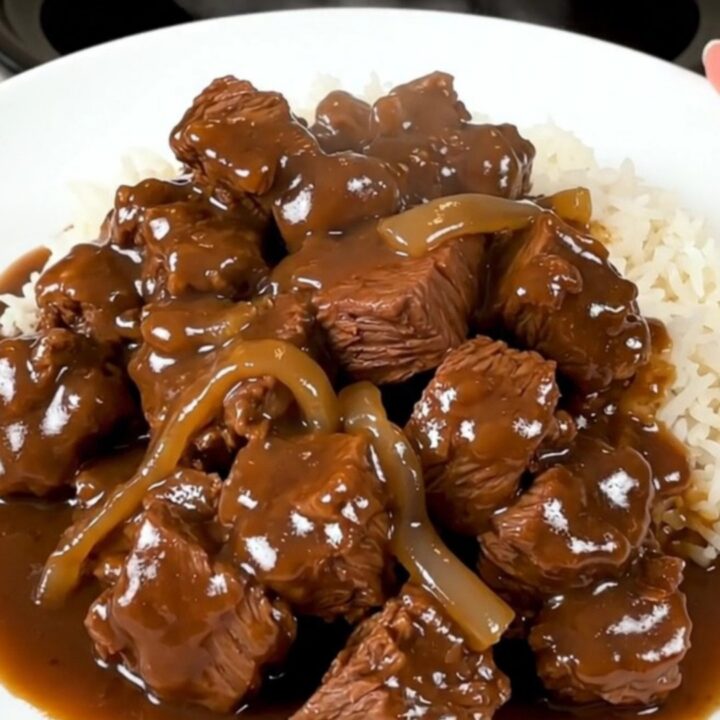 A slow cooker filled with tender beef cubes, thick sweet onion slices, and a rich, savory brown gravy.