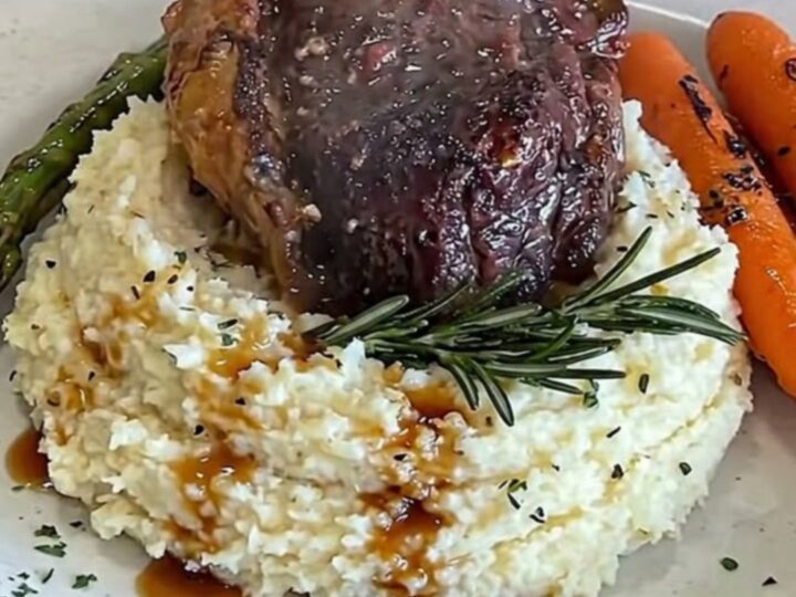 A perfectly glazed filet mignon resting on creamy mashed cauliflower with roasted carrots and asparagus