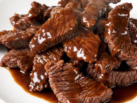 A plate of tender, glossy Szechuan beef with red bell peppers, steaming and ready to eat.