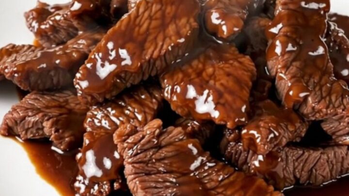 A plate of tender, glossy Szechuan beef with red bell peppers, steaming and ready to eat.