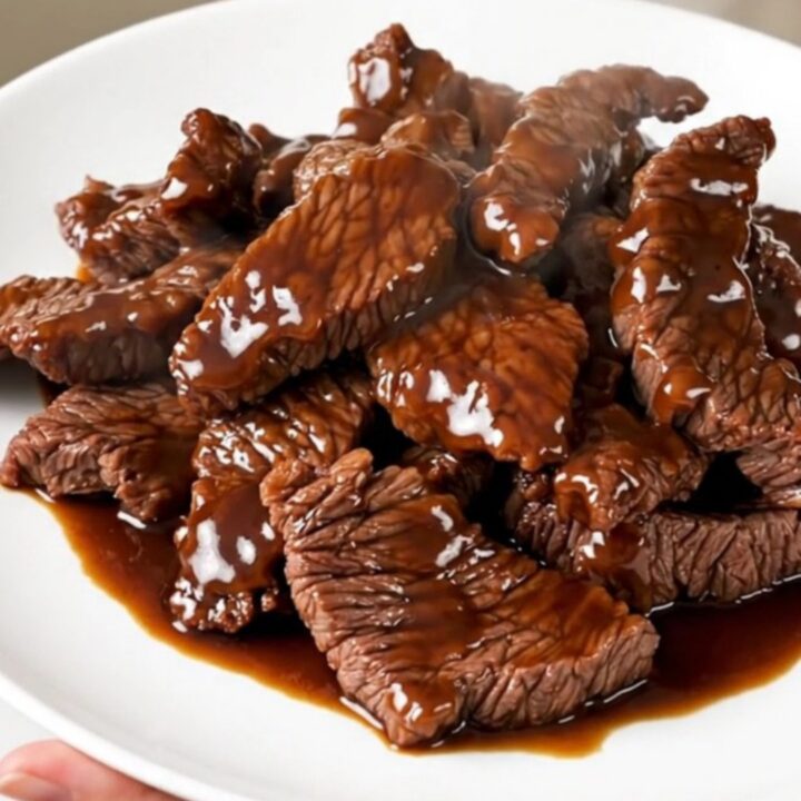 A plate of tender, glossy Szechuan beef with red bell peppers, steaming and ready to eat.