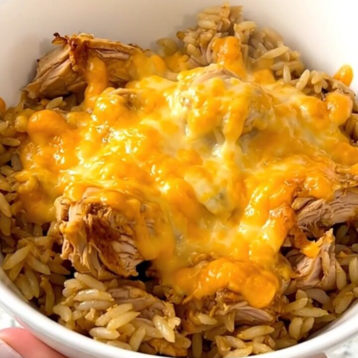 A slow cooker filled with chicken, rice, and salsa verde, topped with melted cheese.