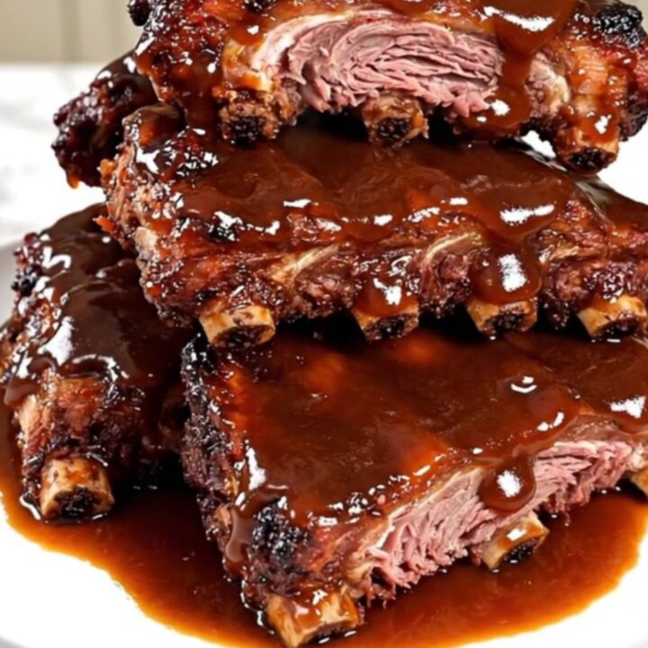 Close-up of glossy, slow-cooked baby back ribs glazed in apple butter sauce on a white plate.