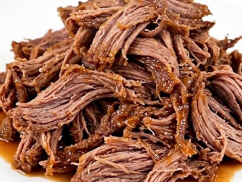 A close-up of a serving plate filled with tender, shredded buffalo beef in a glossy red sauce.