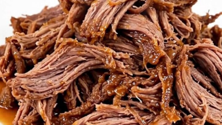A close-up of a serving plate filled with tender, shredded buffalo beef in a glossy red sauce.