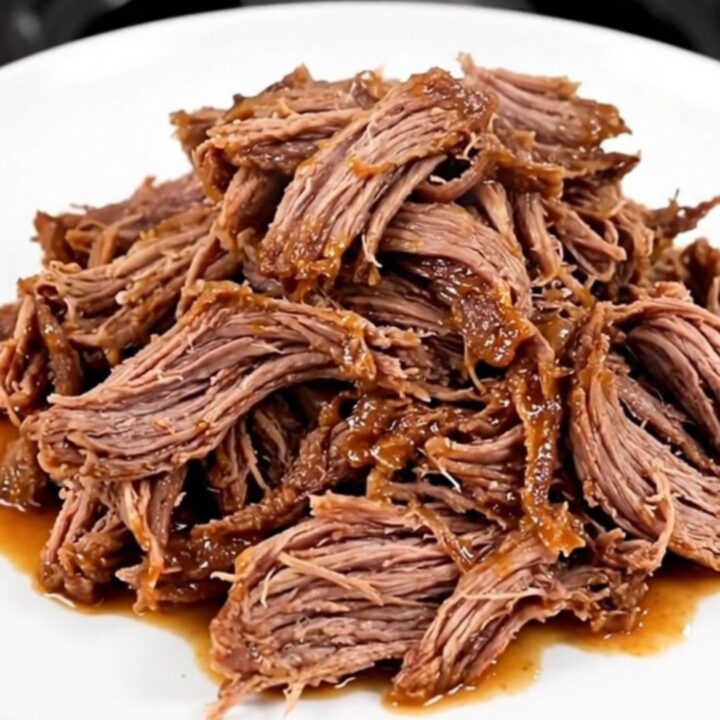 A close-up of a serving plate filled with tender, shredded buffalo beef in a glossy red sauce.