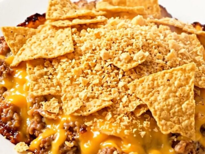 A steaming, hearty ground beef and bean casserole served in a slow cooker, topped with crushed tortilla chips.