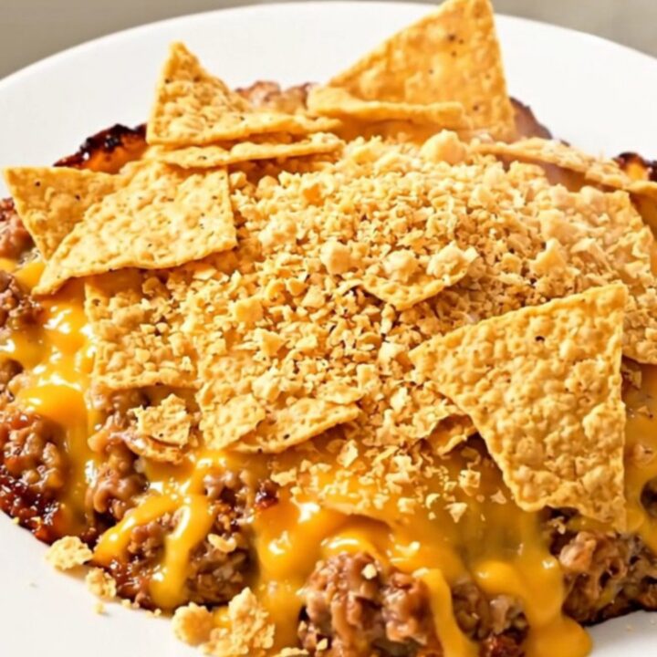 A steaming, hearty ground beef and bean casserole served in a slow cooker, topped with crushed tortilla chips.