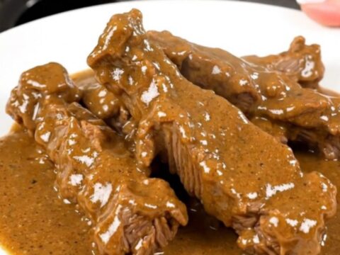 A close-up of tender beef tips in a creamy white sauce with sliced mushrooms on a white plate.