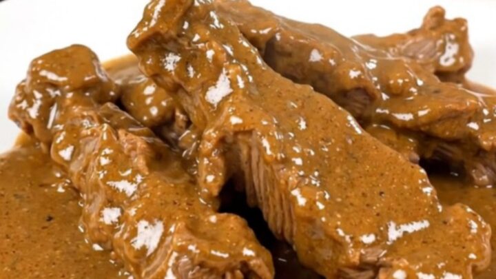 A close-up of tender beef tips in a creamy white sauce with sliced mushrooms on a white plate.