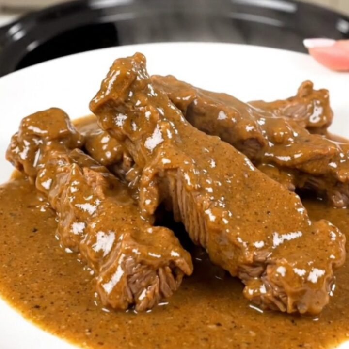 A close-up of tender beef tips in a creamy white sauce with sliced mushrooms on a white plate.