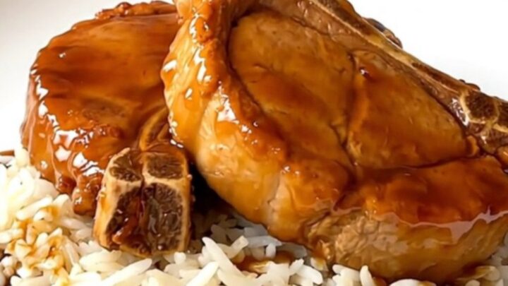 A close overhead view of tender, glazed orange pork chops in a black slow cooker on a white countertop.