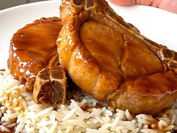 A close overhead view of tender, glazed orange pork chops in a black slow cooker on a white countertop.