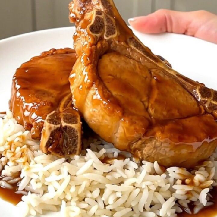 A close overhead view of tender, glazed orange pork chops in a black slow cooker on a white countertop.