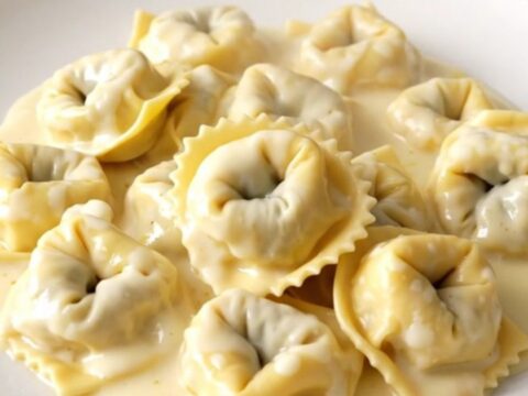 A top-down view of a black slow cooker filled with creamy alfredo tortellini, showing the rich sauce and tender pasta.