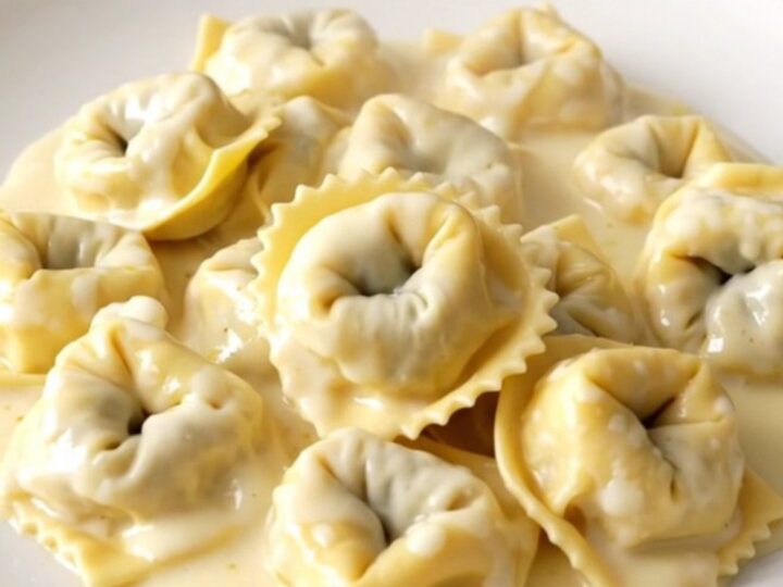 A top-down view of a black slow cooker filled with creamy alfredo tortellini, showing the rich sauce and tender pasta.
