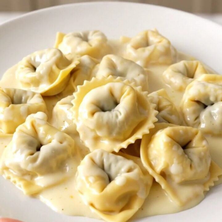 A top-down view of a black slow cooker filled with creamy alfredo tortellini, showing the rich sauce and tender pasta.