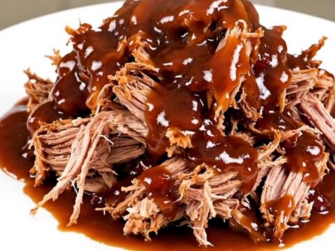 Tender pulled pork piled high on a white plate, showing a rich cranberry barbecue glaze.