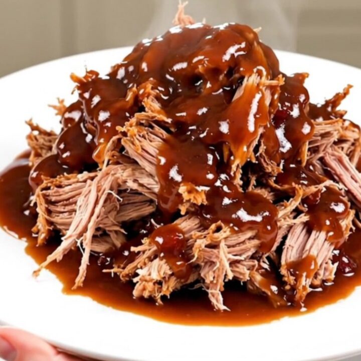 Tender pulled pork piled high on a white plate, showing a rich cranberry barbecue glaze.