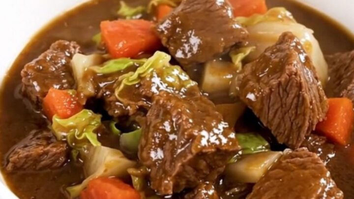 A top-down view of a black slow cooker filled with raw beef, cabbage, and carrots waiting to be cooked.