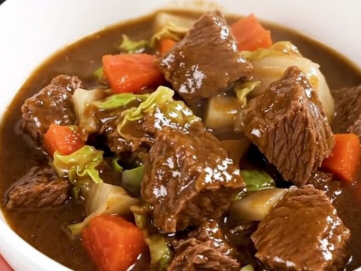 A top-down view of a black slow cooker filled with raw beef, cabbage, and carrots waiting to be cooked.