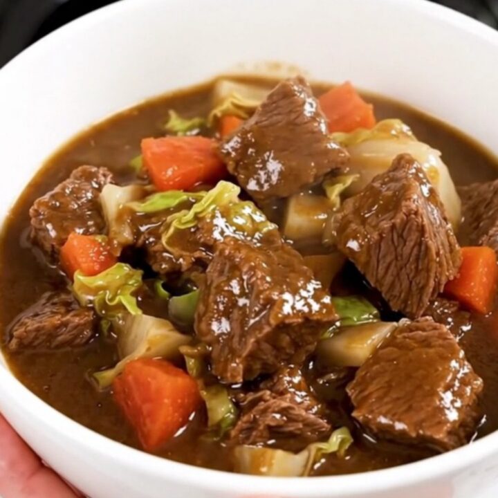 A top-down view of a black slow cooker filled with raw beef, cabbage, and carrots waiting to be cooked.