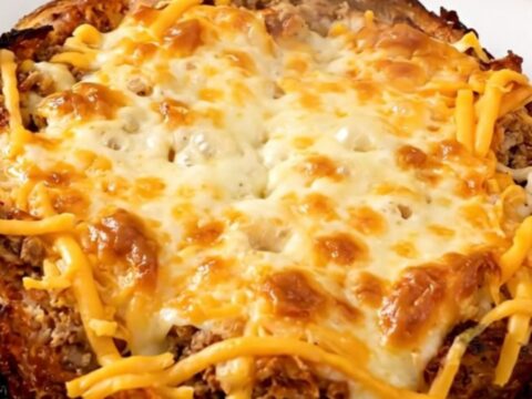 A top-down shot of a slow cooker filled with a savory beef and bean burrito casserole, topped with melted cheese.