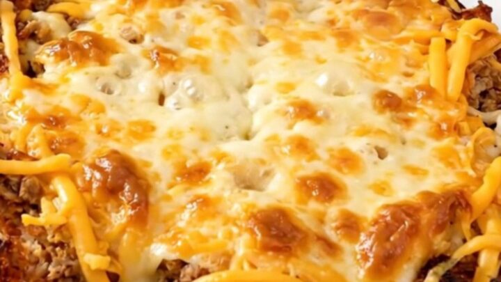 A top-down shot of a slow cooker filled with a savory beef and bean burrito casserole, topped with melted cheese.