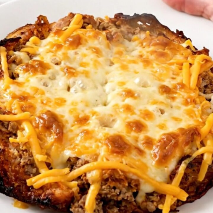 A top-down shot of a slow cooker filled with a savory beef and bean burrito casserole, topped with melted cheese.
