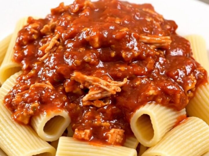 A rustic bowl of slow-cooked turkey bolognese served over rigatoni pasta, topped with fresh herbs.