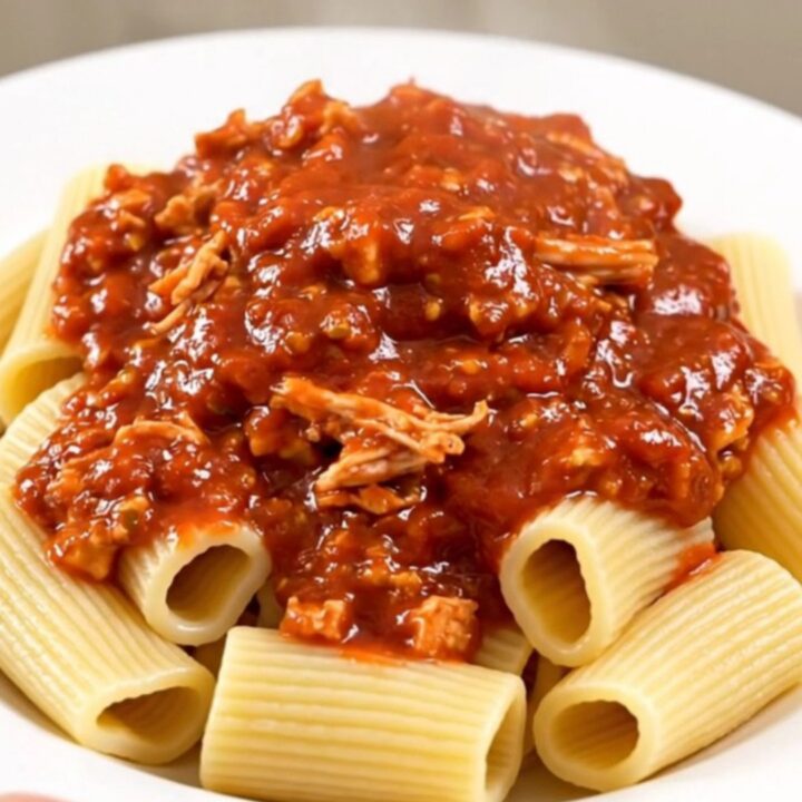 A rustic bowl of slow-cooked turkey bolognese served over rigatoni pasta, topped with fresh herbs.