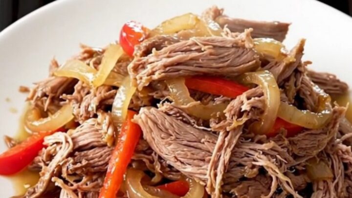 A close-up of a tender shredded Cajun pot roast with colorful bell peppers and onions in a slow cooker.