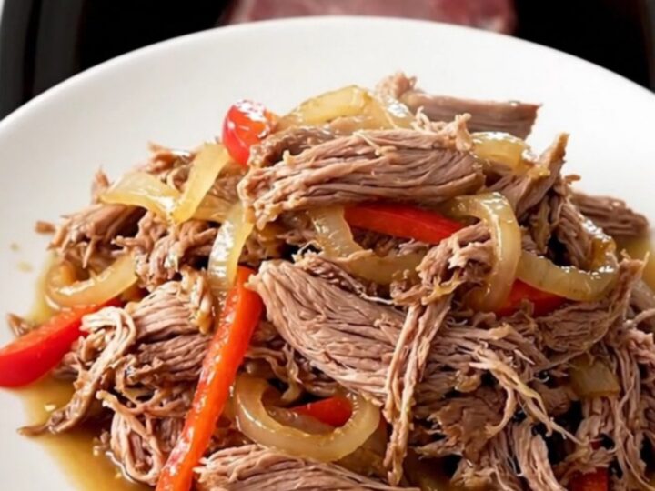 A close-up of a tender shredded Cajun pot roast with colorful bell peppers and onions in a slow cooker.
