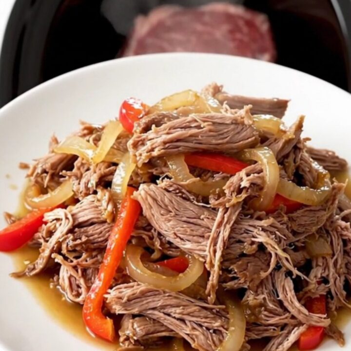 A close-up of a tender shredded Cajun pot roast with colorful bell peppers and onions in a slow cooker.