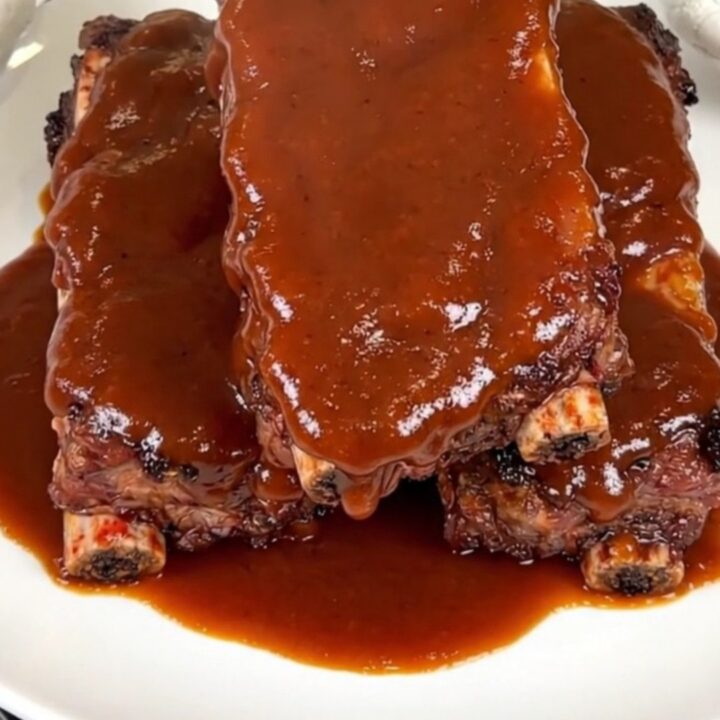 A close-up of glossy, smoky chipotle barbecue ribs on a white plate.