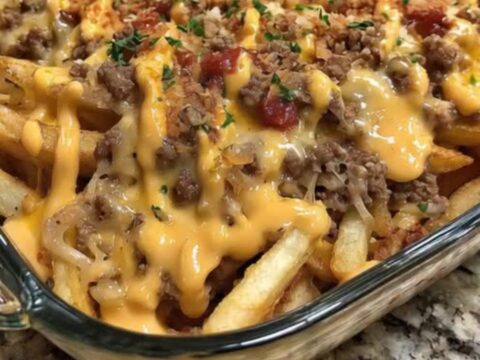 A spatula scooping into a golden cheeseburger french fry casserole, lifting melted cheddar and crispy fries.
