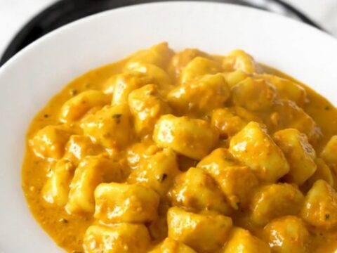 A top-down view of a slow cooker filled with creamy pumpkin alfredo gnocchi on a white speckled countertop.