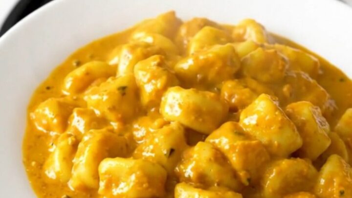 A top-down view of a slow cooker filled with creamy pumpkin alfredo gnocchi on a white speckled countertop.